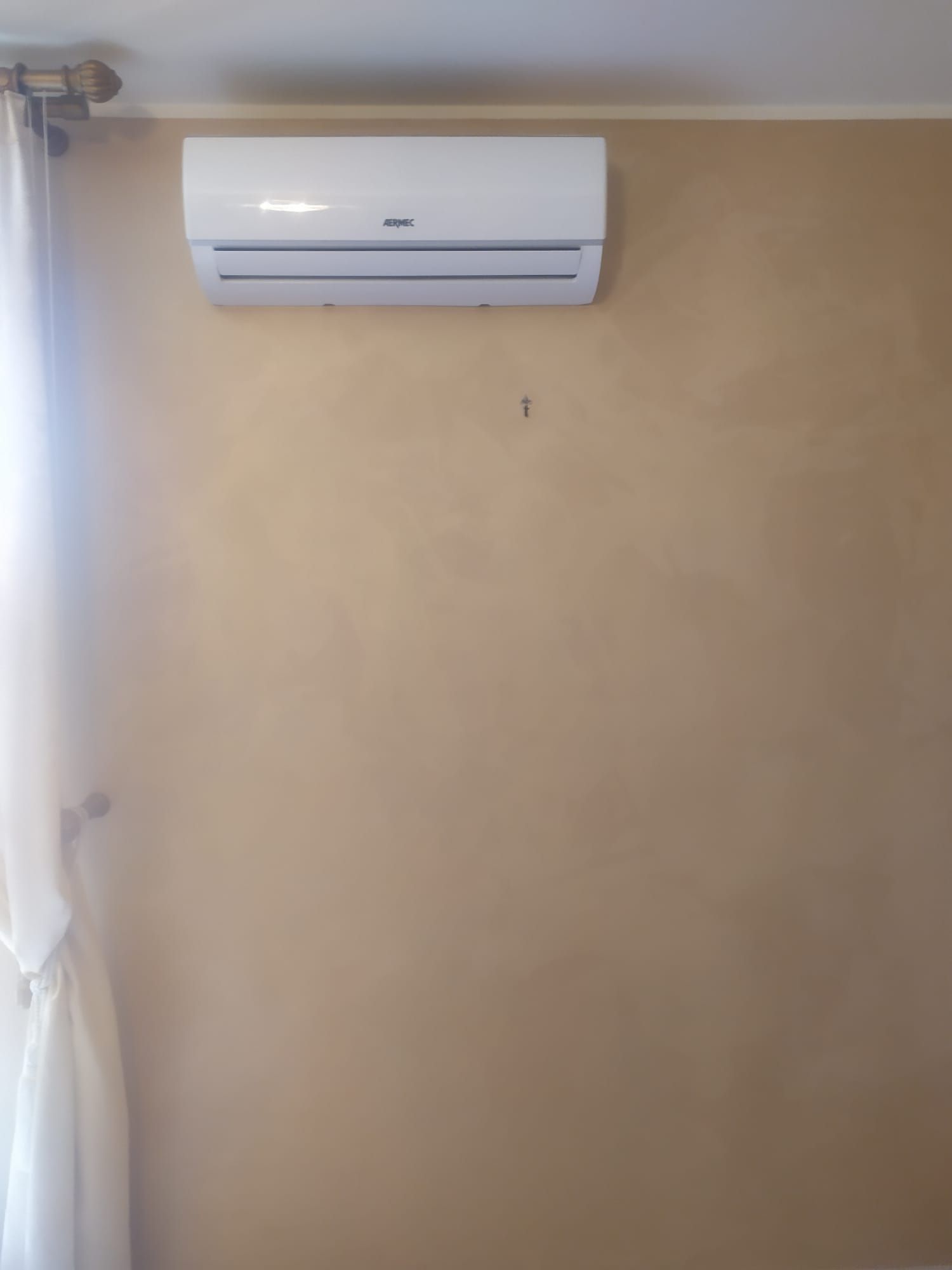 Un condizionatore bianco è appeso a una parete marrone chiaro accanto a una finestra.