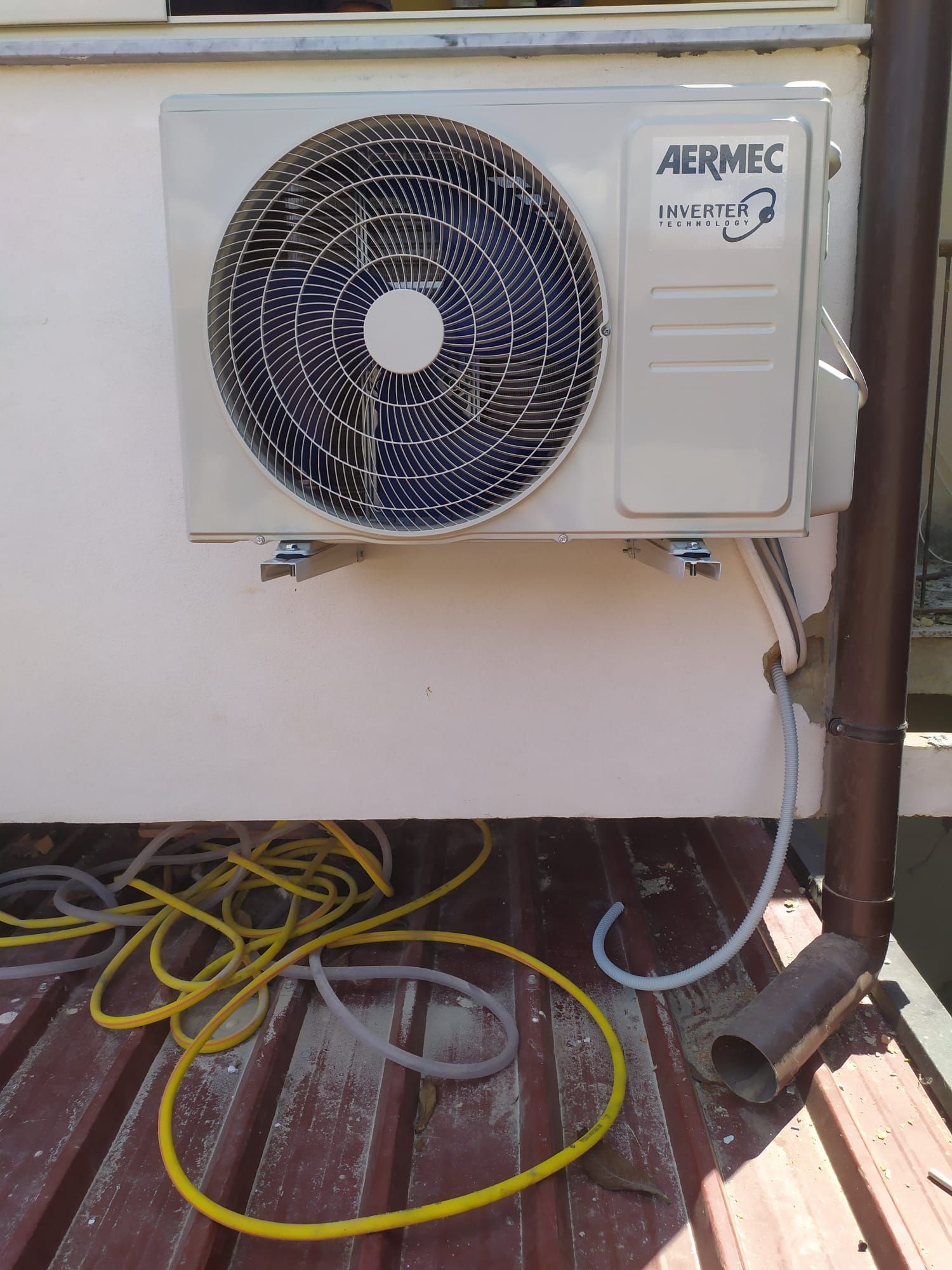 Un condizionatore bianco è appoggiato su una terrazza di legno accanto a un tubo flessibile giallo.