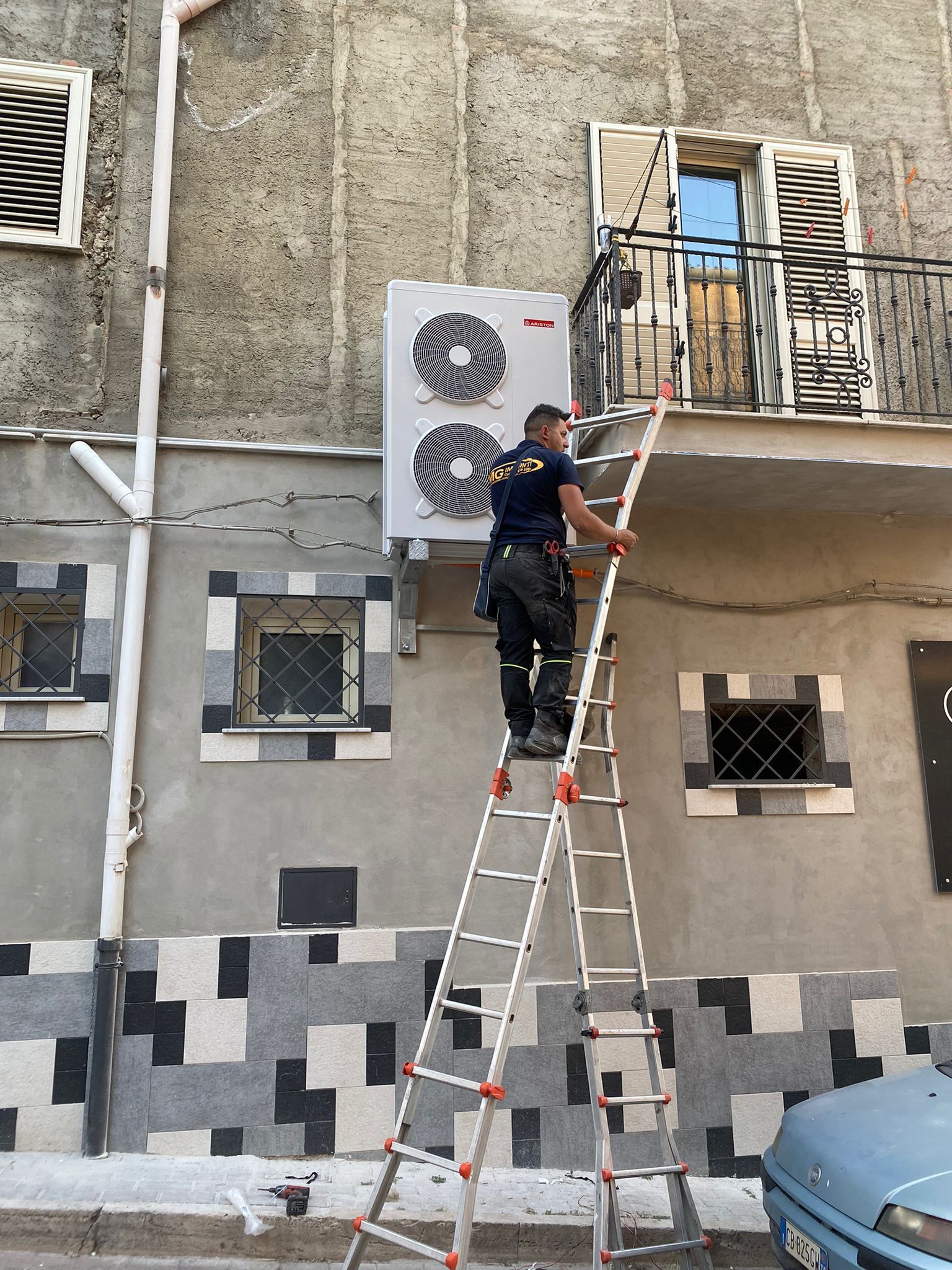 Un uomo sta salendo una scala per installare un condizionatore d'aria sulla facciata di un edificio.