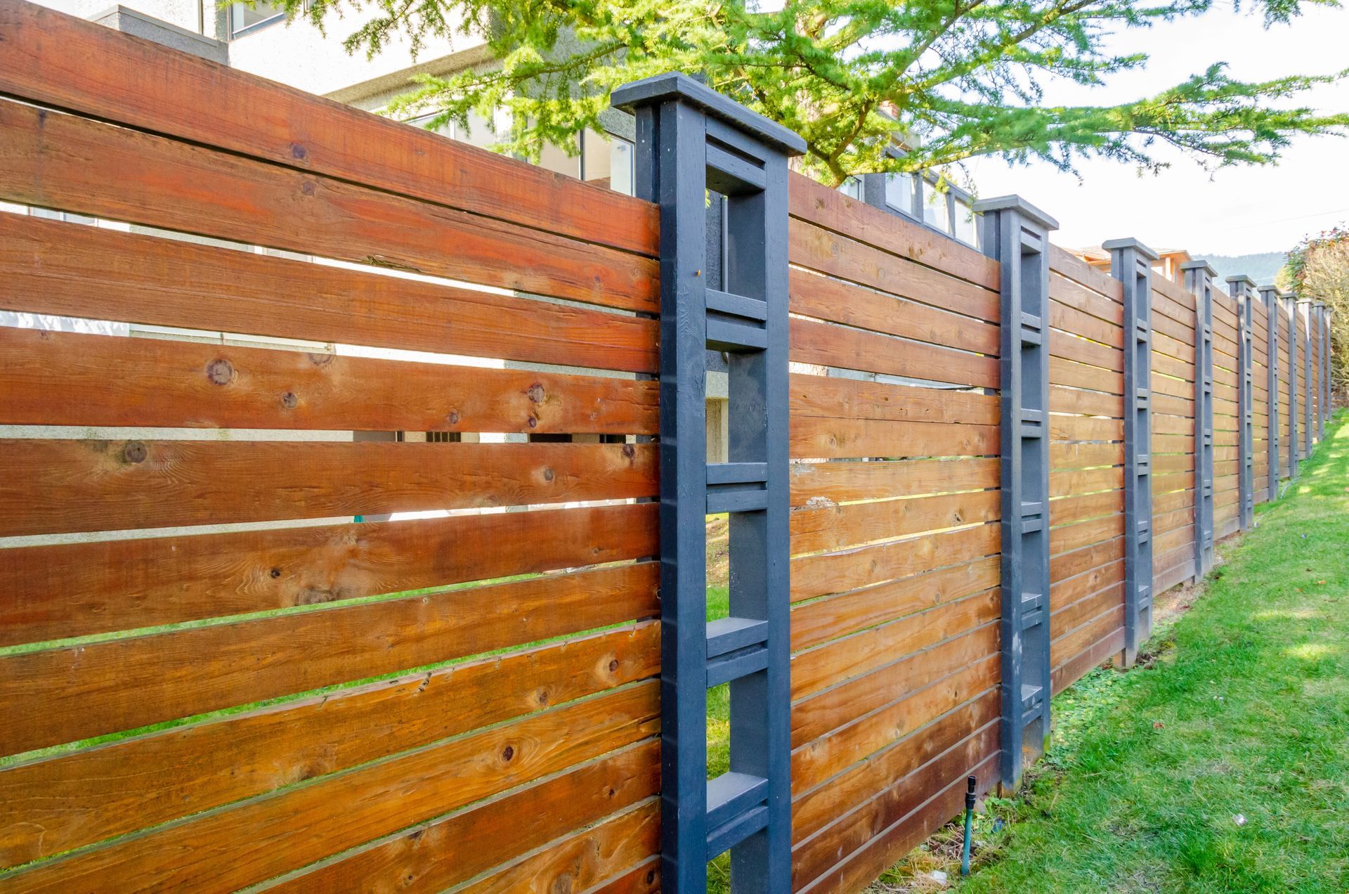A wooden fence with a black post in the middle of a yard.