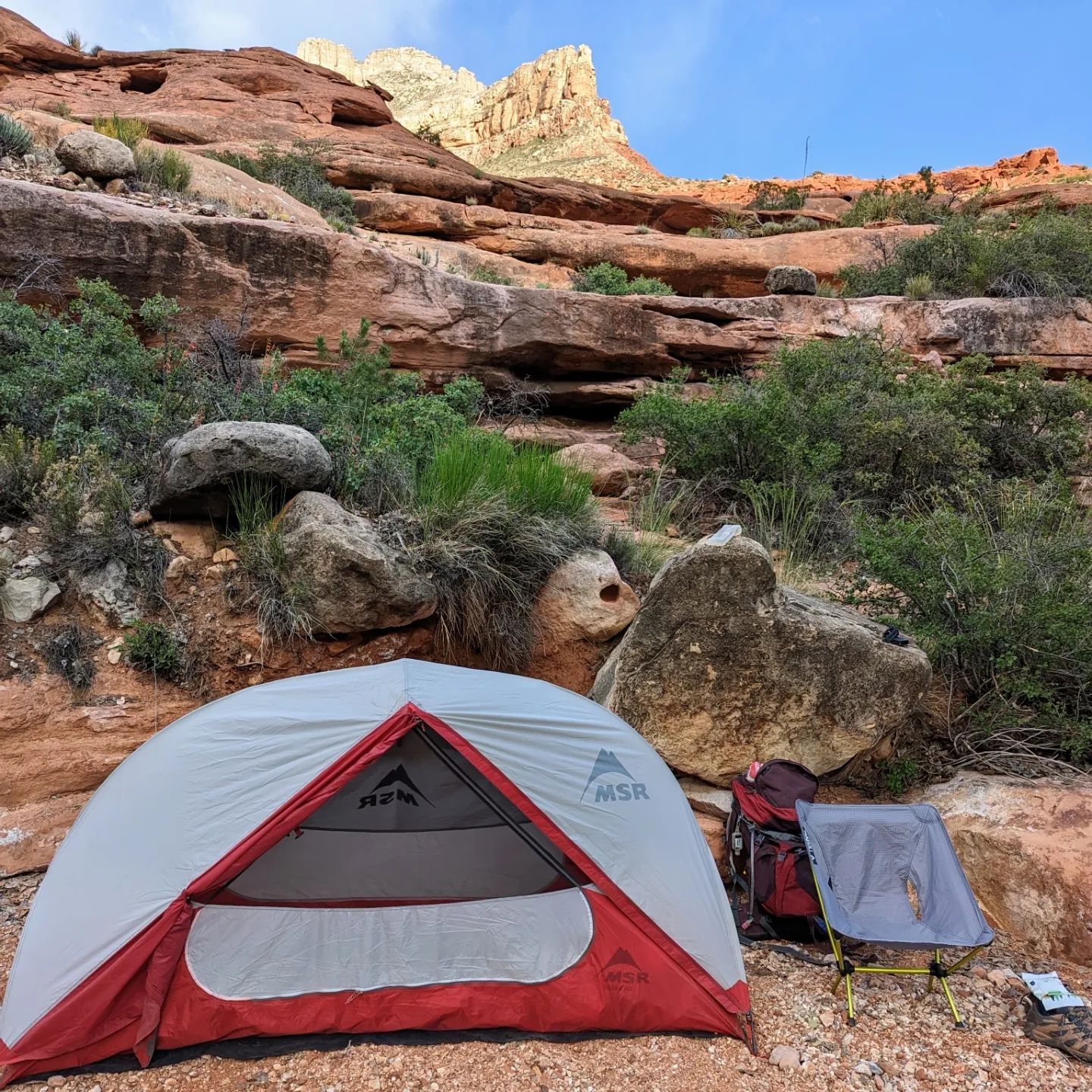A red and white tent is sitting on top of a rocky hillside.