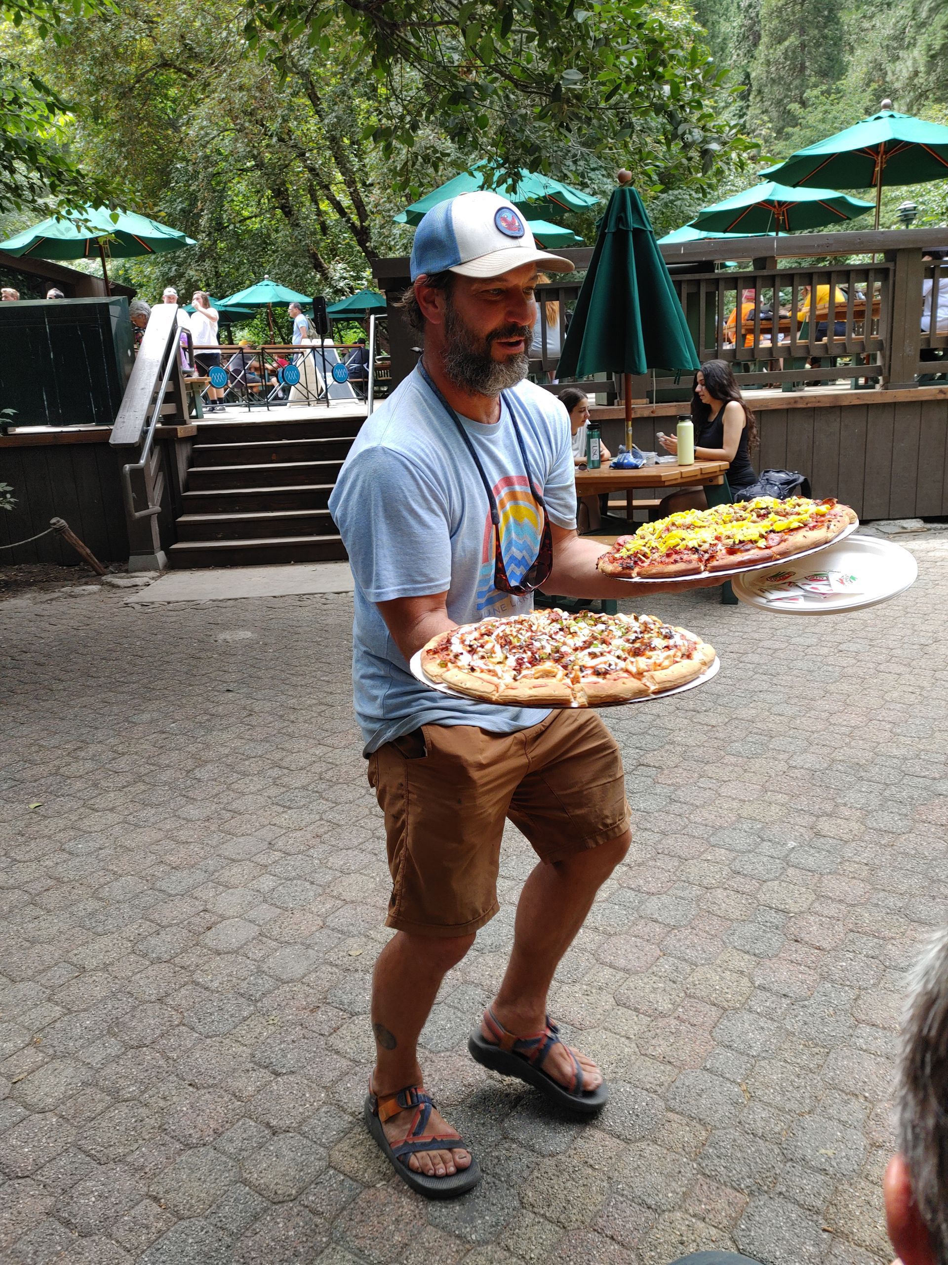 A man is holding two plates of pizza in his hands.