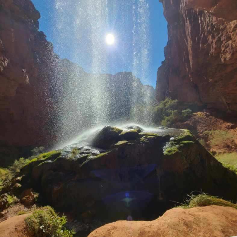 A waterfall in a canyon with the sun shining through it