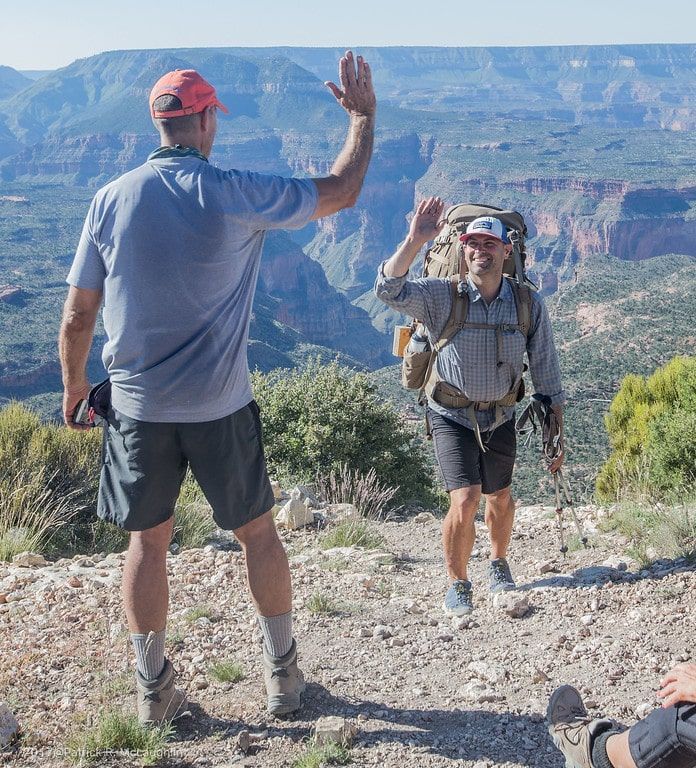 A man with a backpack is giving a high five to another man