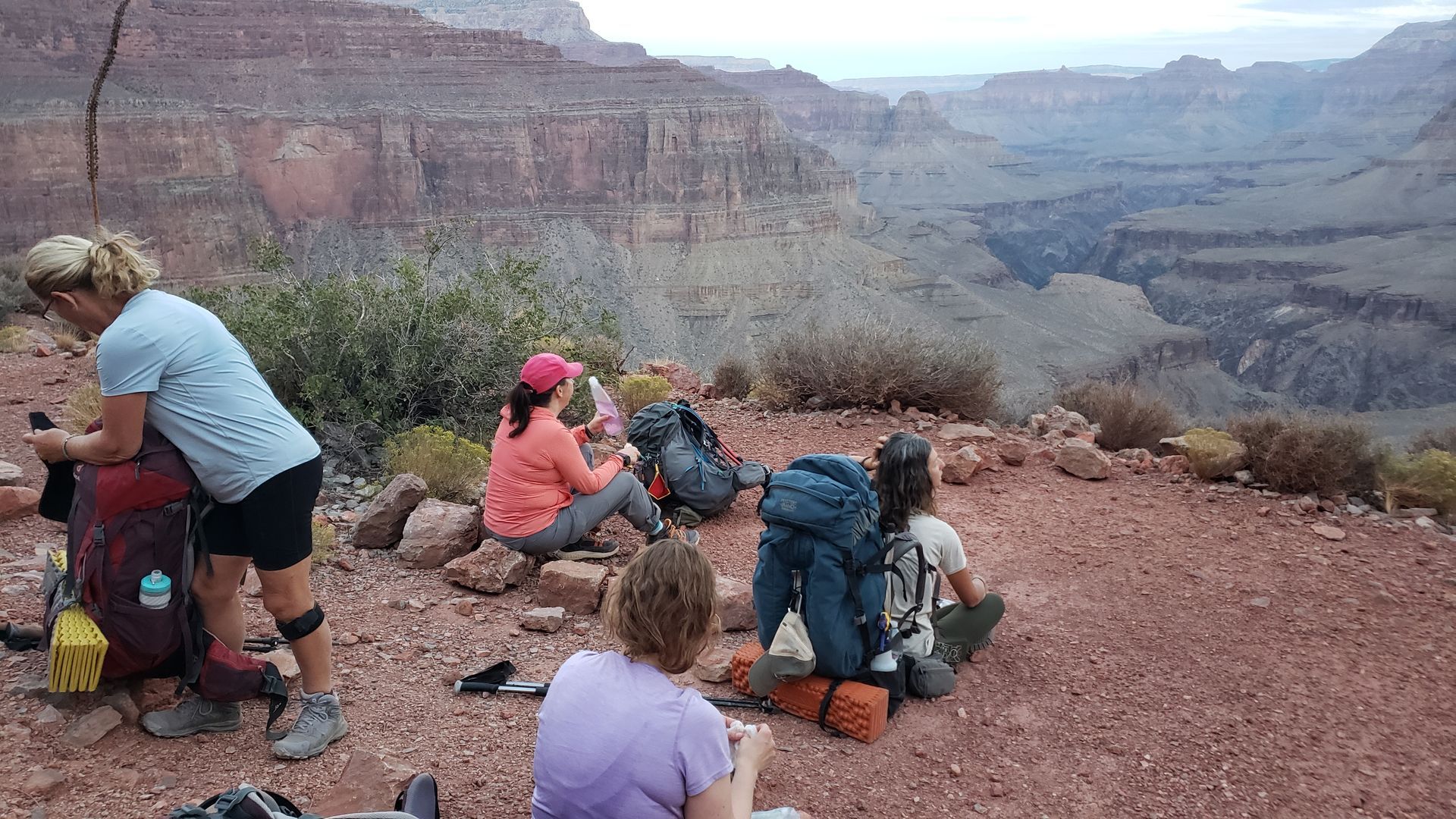 A group of people are sitting on top of a rocky hill overlooking a canyon.
