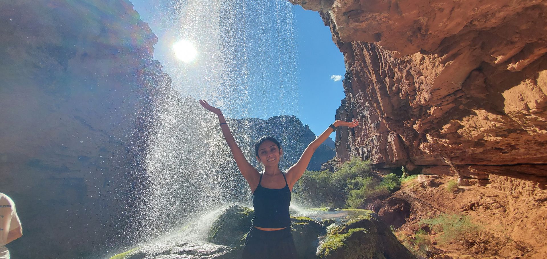 A woman is standing in front of a waterfall with her arms outstretched.