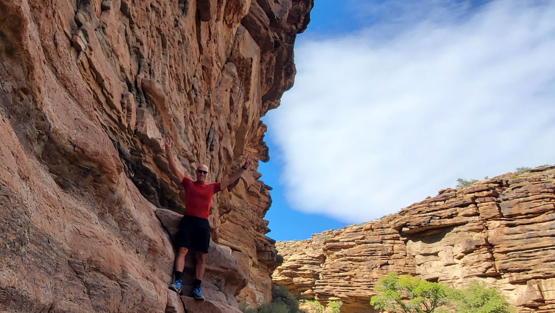 A man in a red shirt is climbing up a rock wall.