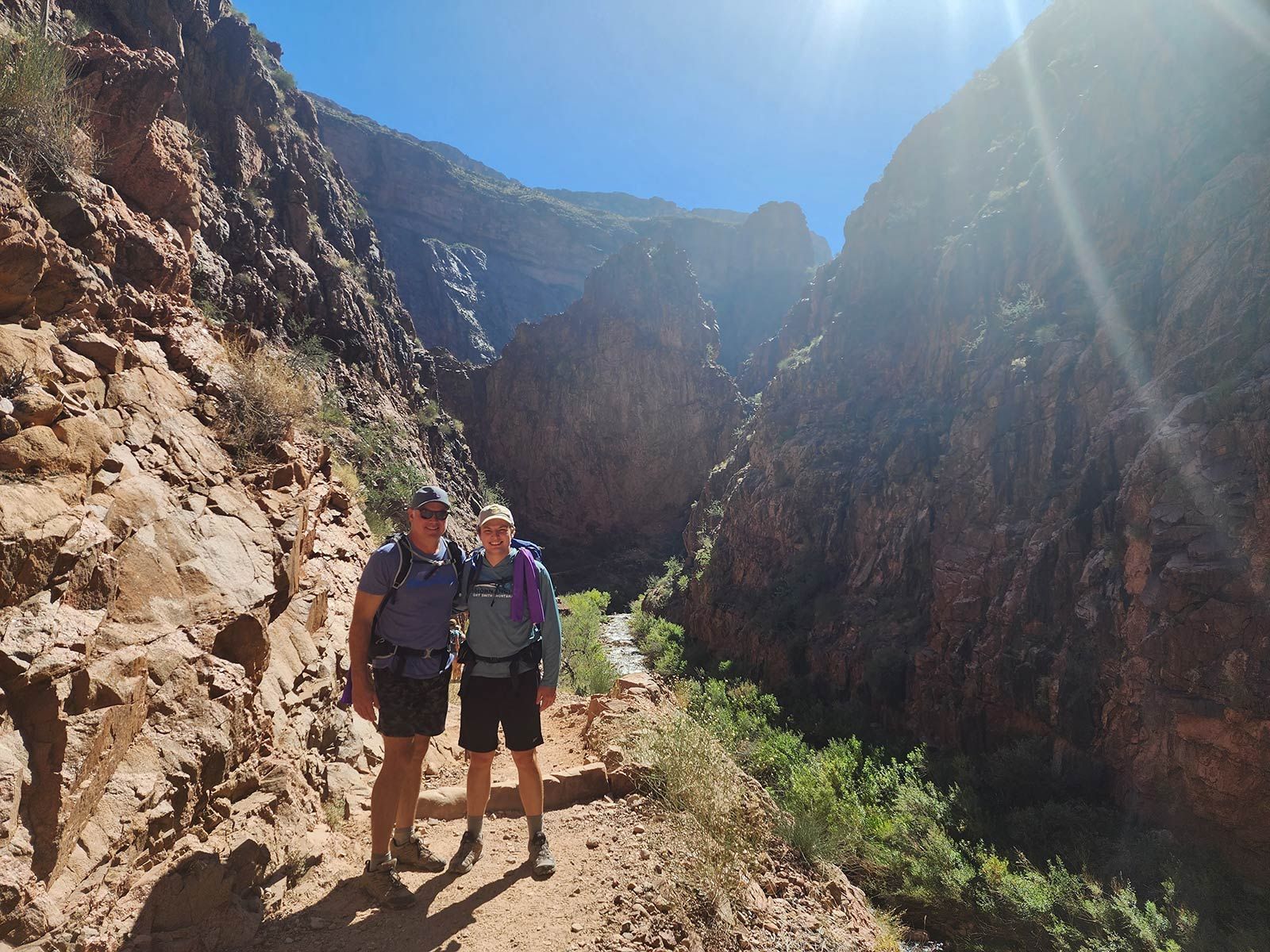 Two people are standing next to each other on a dirt path in the mountains.