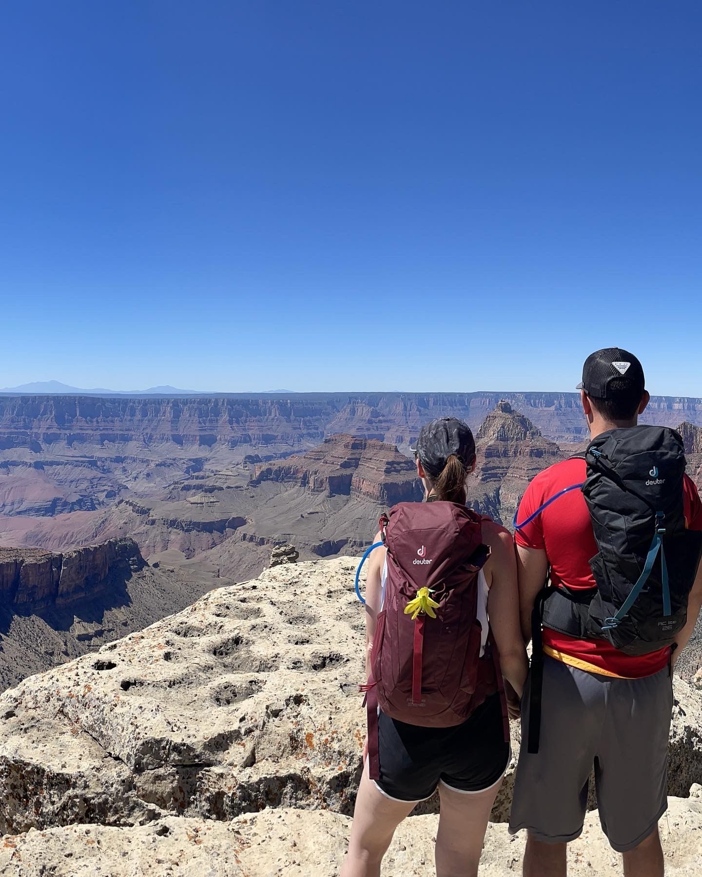 A man and a woman are standing on top of a mountain looking at the grand canyon.