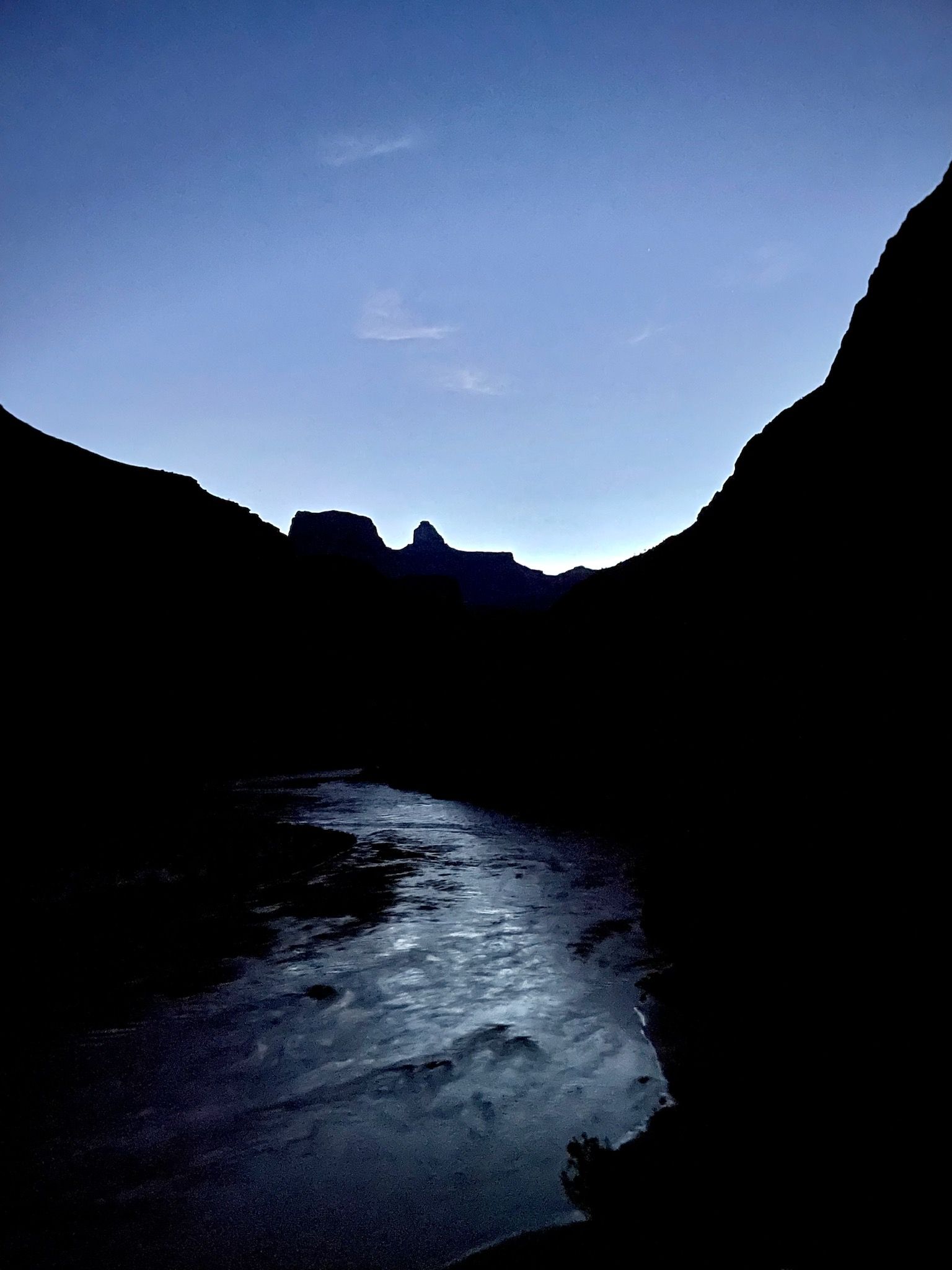 A river flowing through a dark valley with mountains in the background