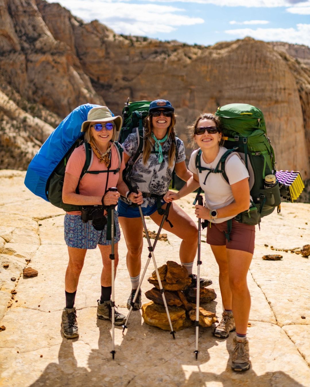 Three women with backpacks and hiking poles are posing for a picture.