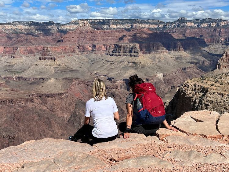 Two people are sitting on top of a rock overlooking a canyon.