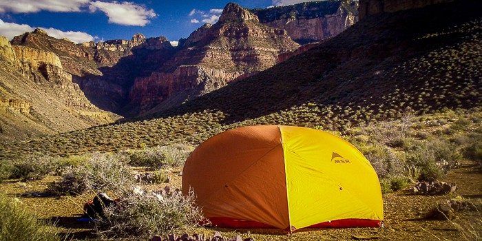 A yellow tent is sitting in the middle of a desert in front of a mountain.