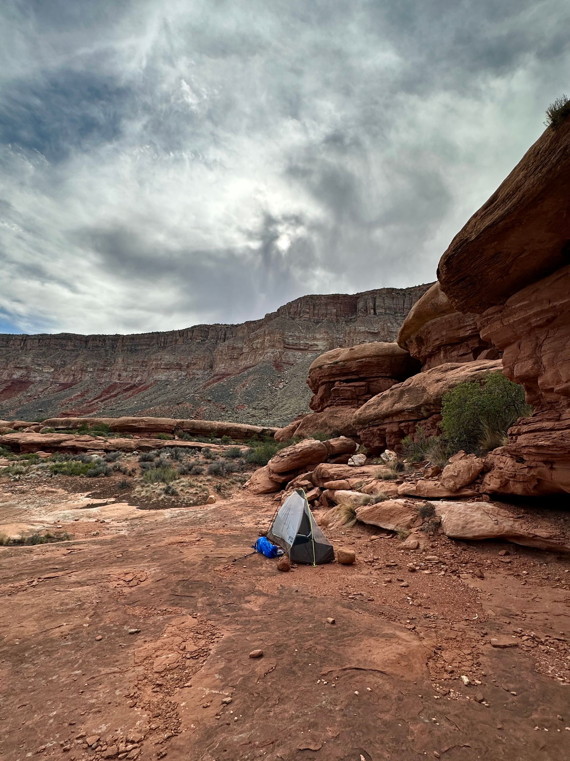 Person camping in a desert landscape with red rocks and cloudy sky.