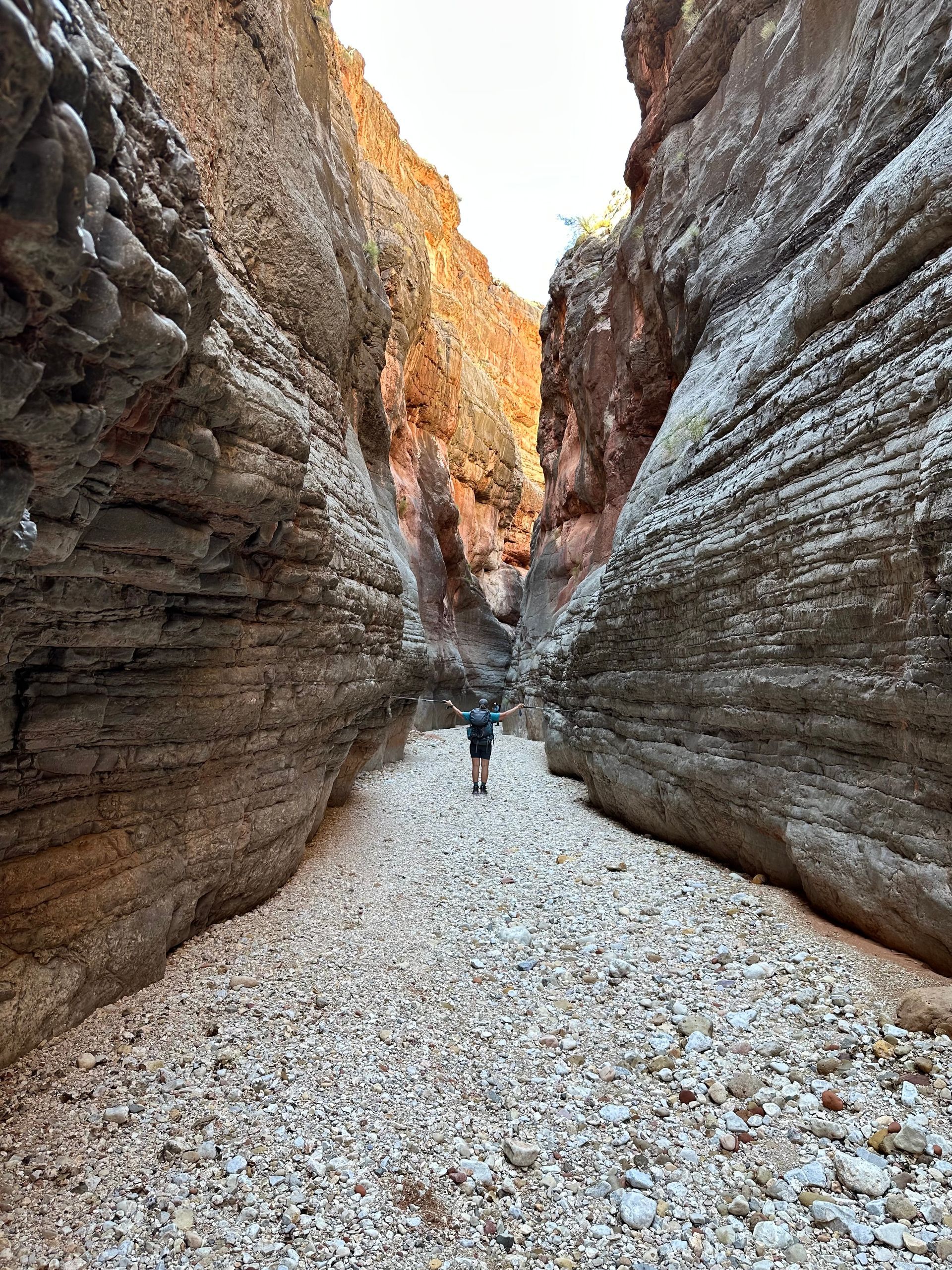 Person standing in a narrow slot canyon with layered, tan-colored rock walls.