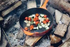 A frying pan filled with vegetables is cooking over a fire