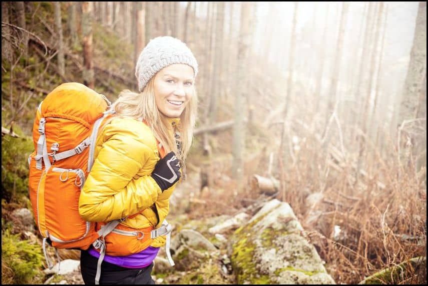 A woman is hiking in the woods with an orange backpack.