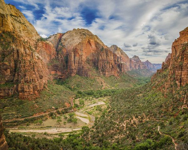 Red canyon cliffs and green valley under a cloudy sky, with a winding river below