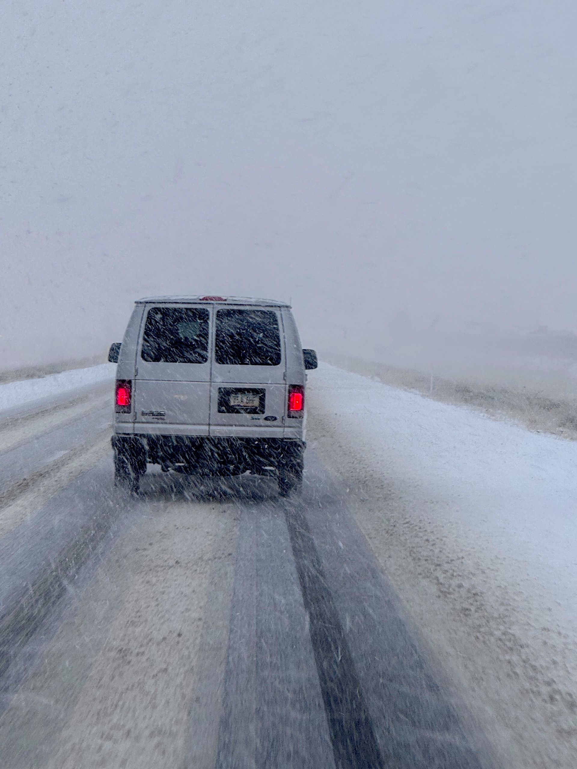 Van driving on snowy road during a blizzard, visibility low.