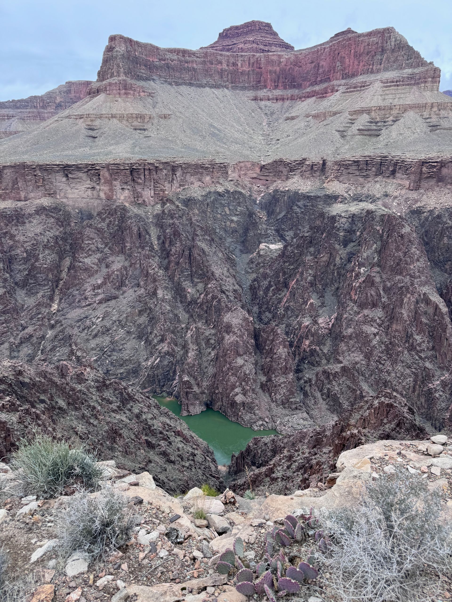 Canyon landscape with layered rock formations and a green body of water in the depths.