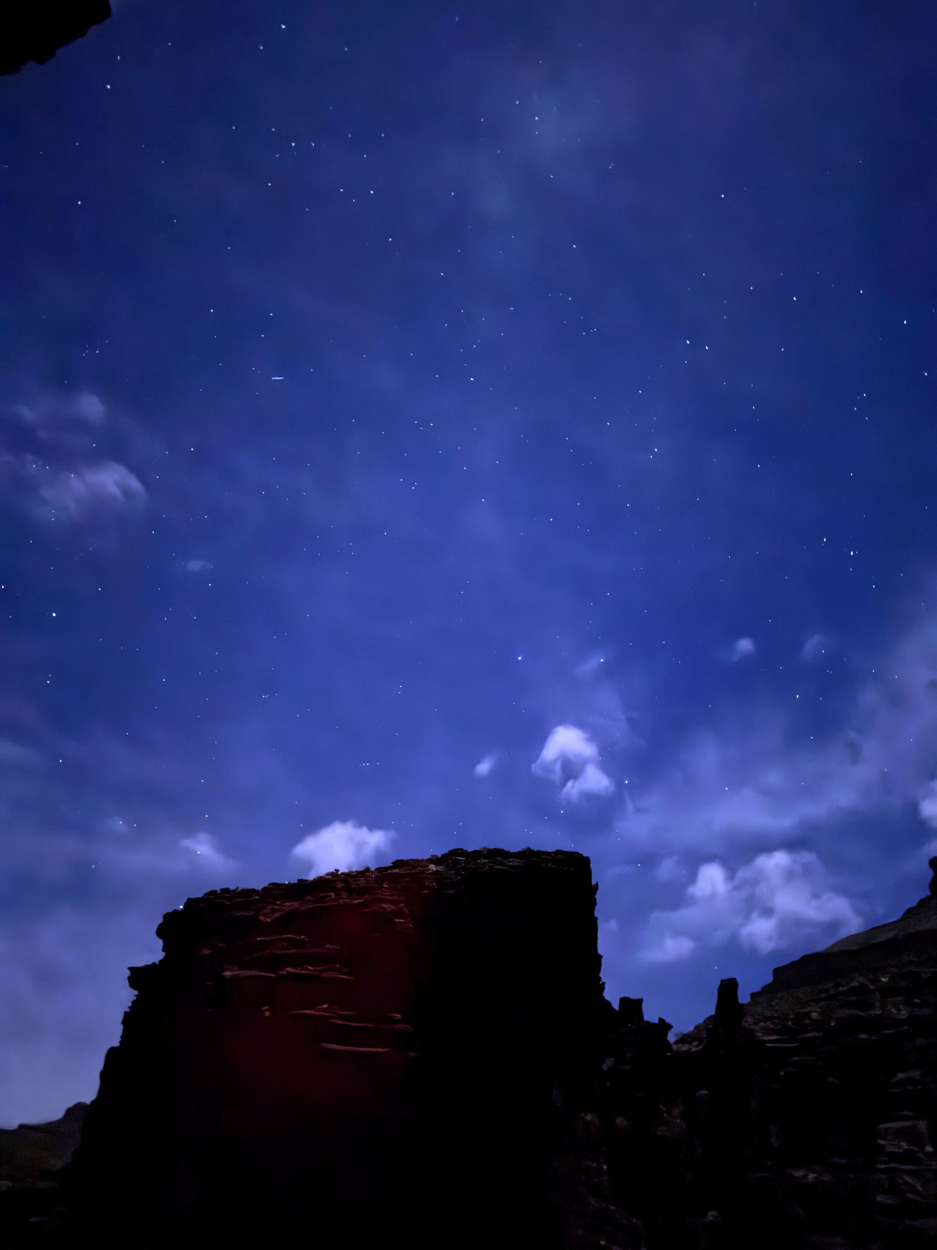 Starry night sky over a dark, silhouetted stone structure. Blue and white clouds.