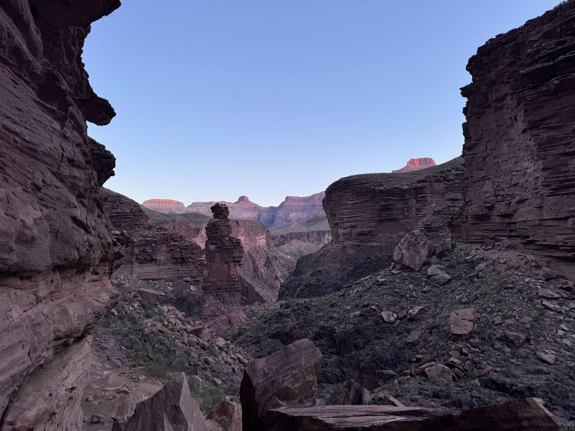 Canyon landscape with rocky walls and distant mesas under a clear blue sky.