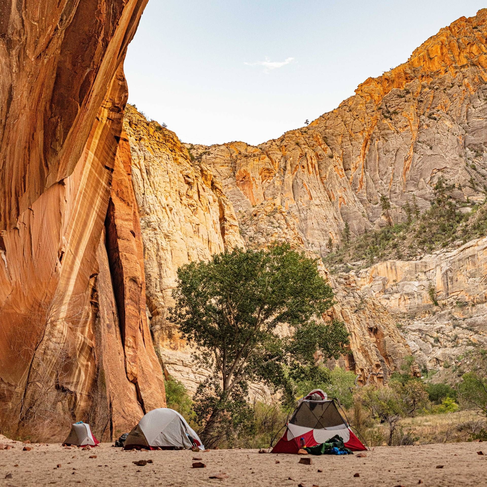 People with backpacks are hiking down a trail next to a cliff.