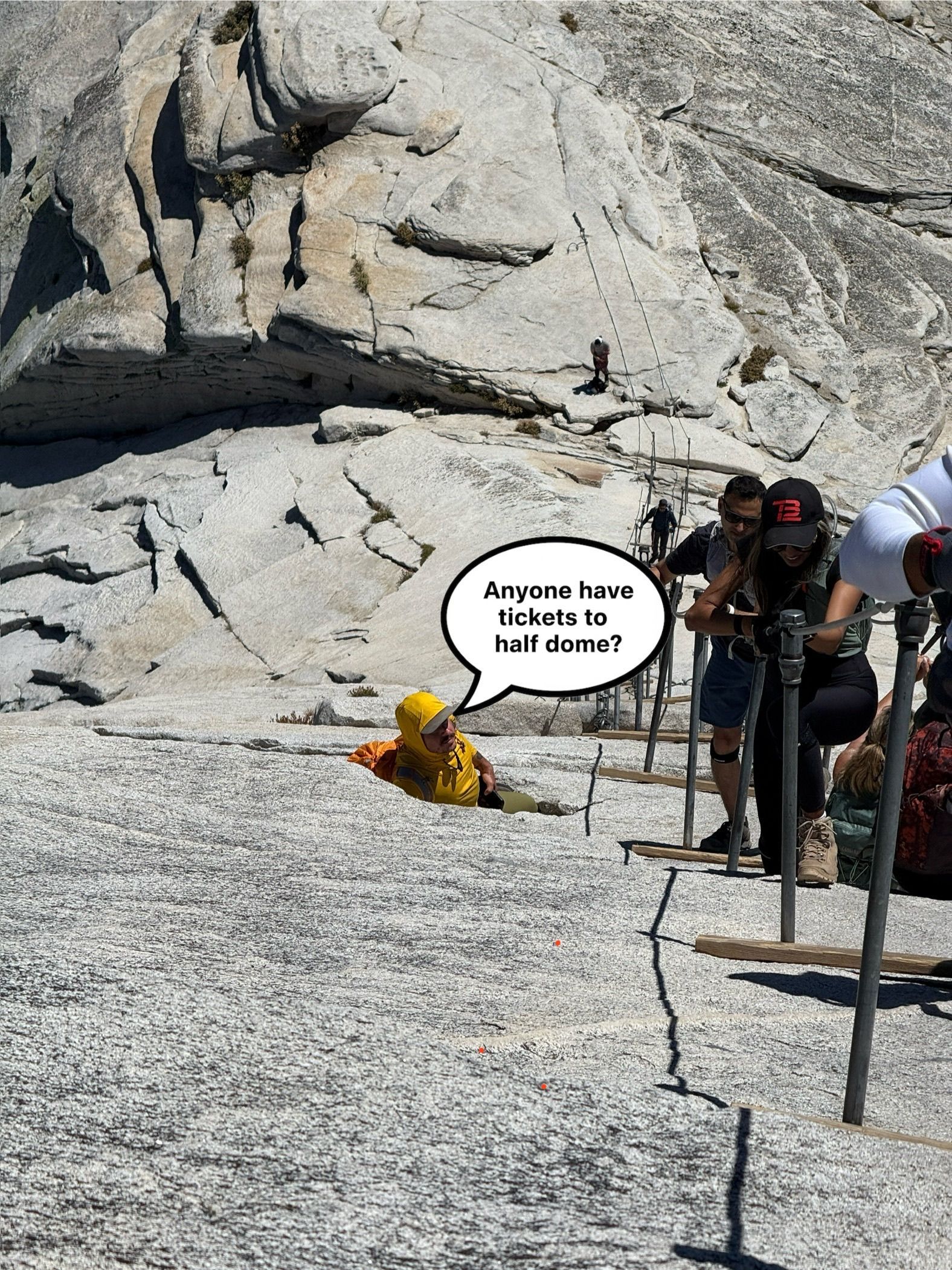 People climbing steep granite with metal handrails. One person in yellow jacket sits near crack.