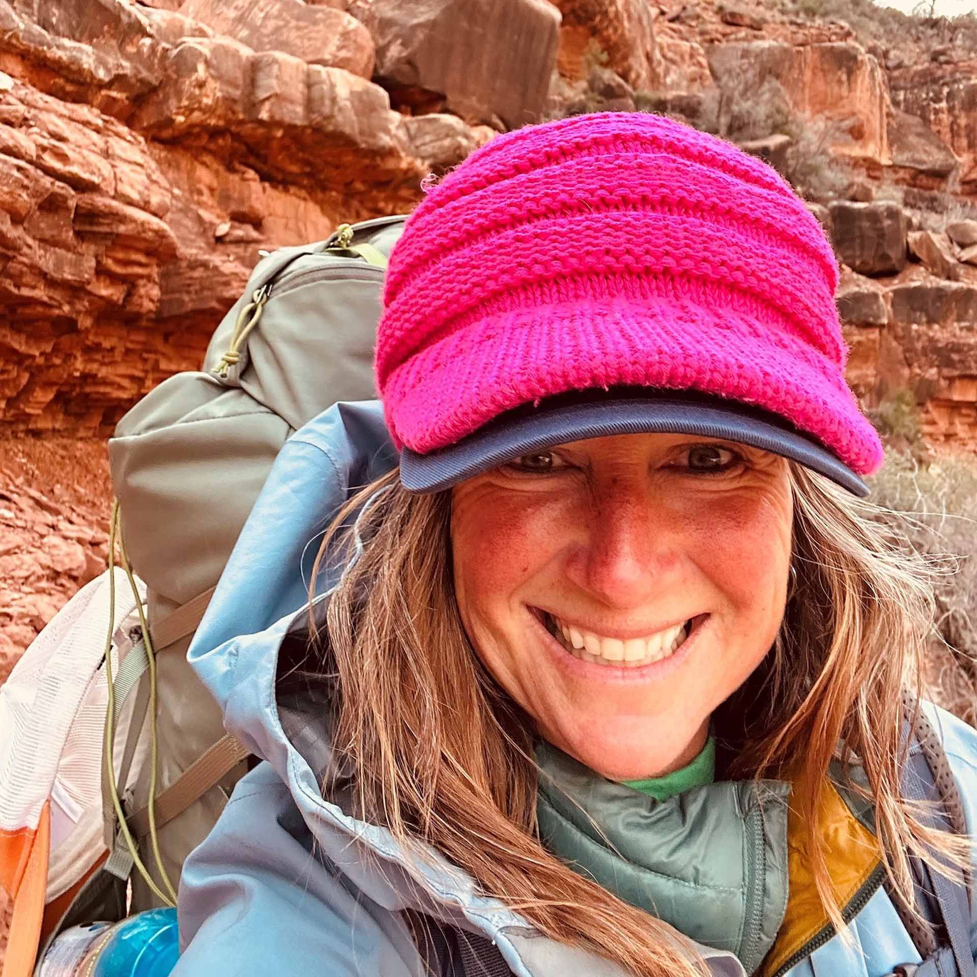 A woman wearing a pink hat and a backpack is smiling