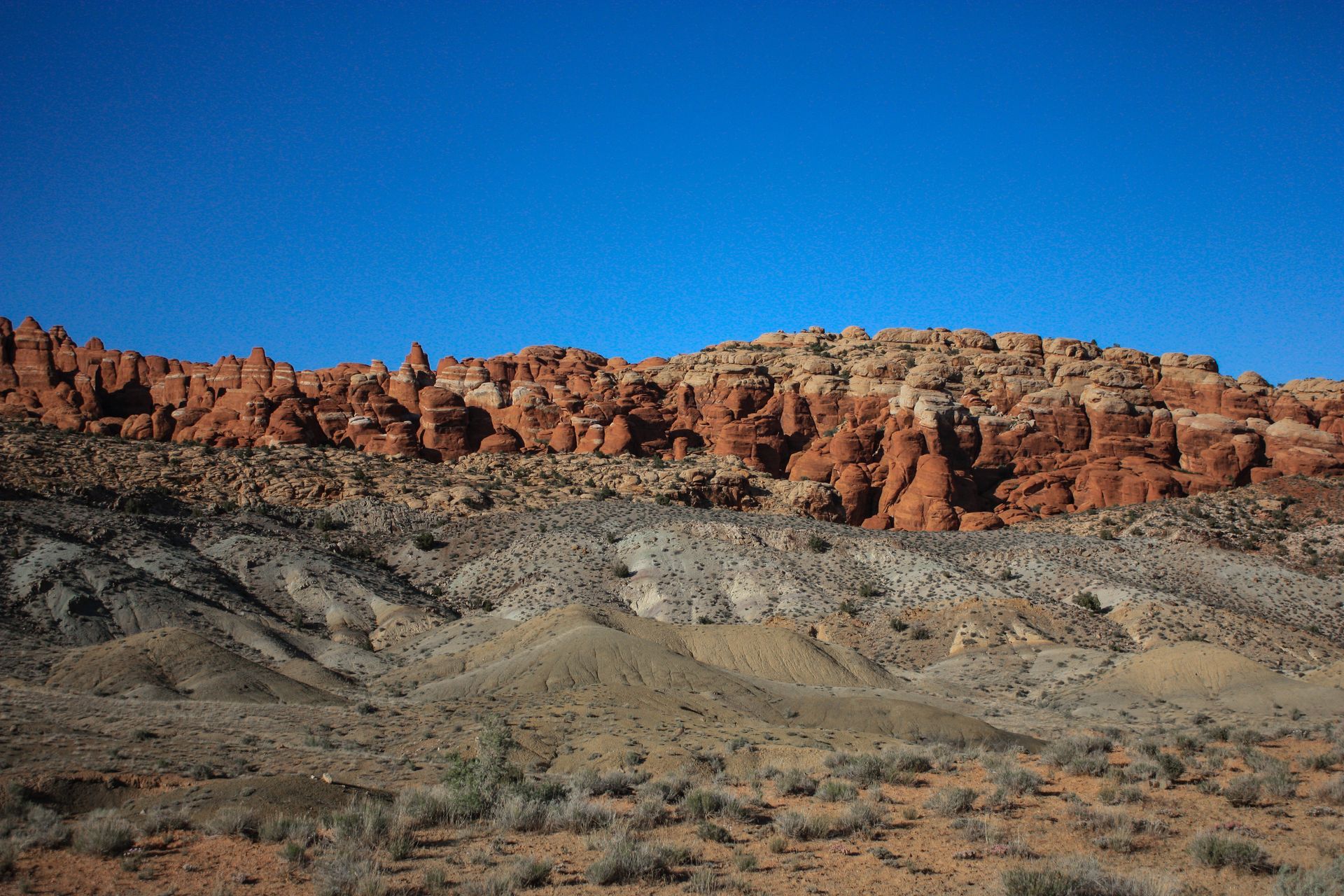 A desert landscape with a mountain in the background and a blue sky