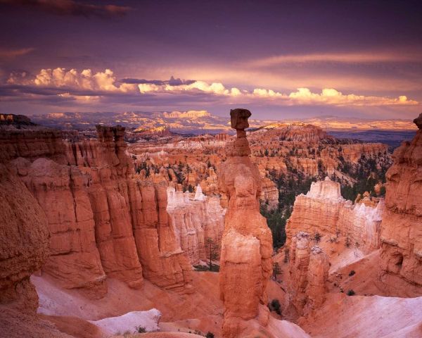 Sunset over red rock canyon cliffs with a tall hoodoo beneath glowing clouds