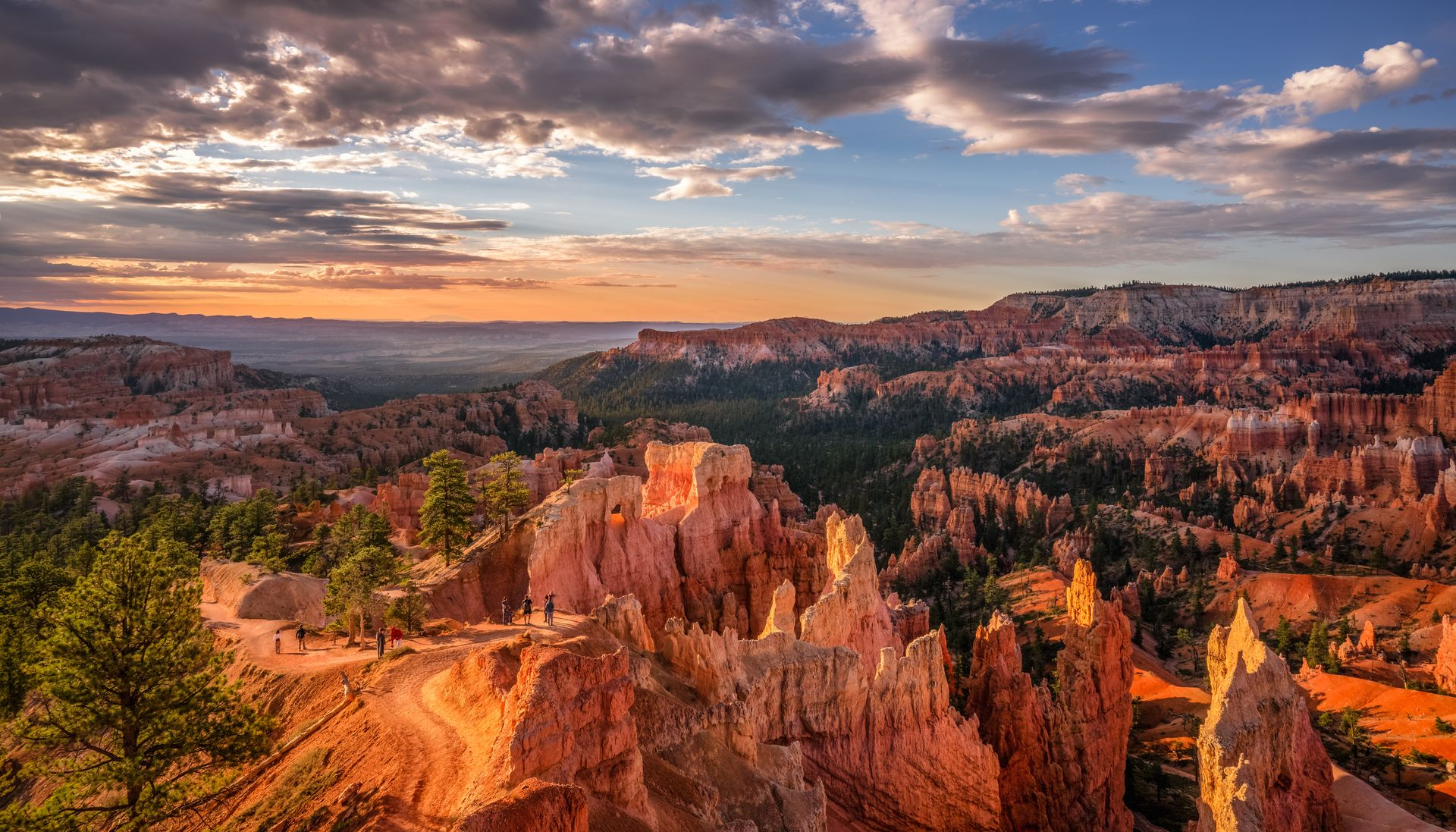 Orange rock formations with green trees under a colorful sunset sky.