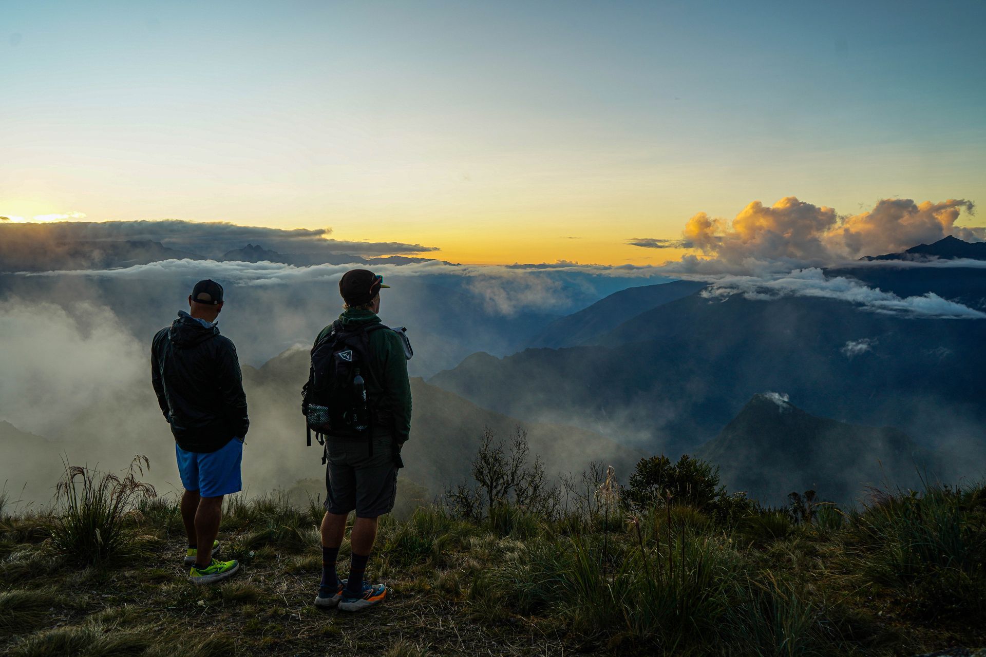 Two hikers overlooking a mountain range at sunset, bathed in golden light.