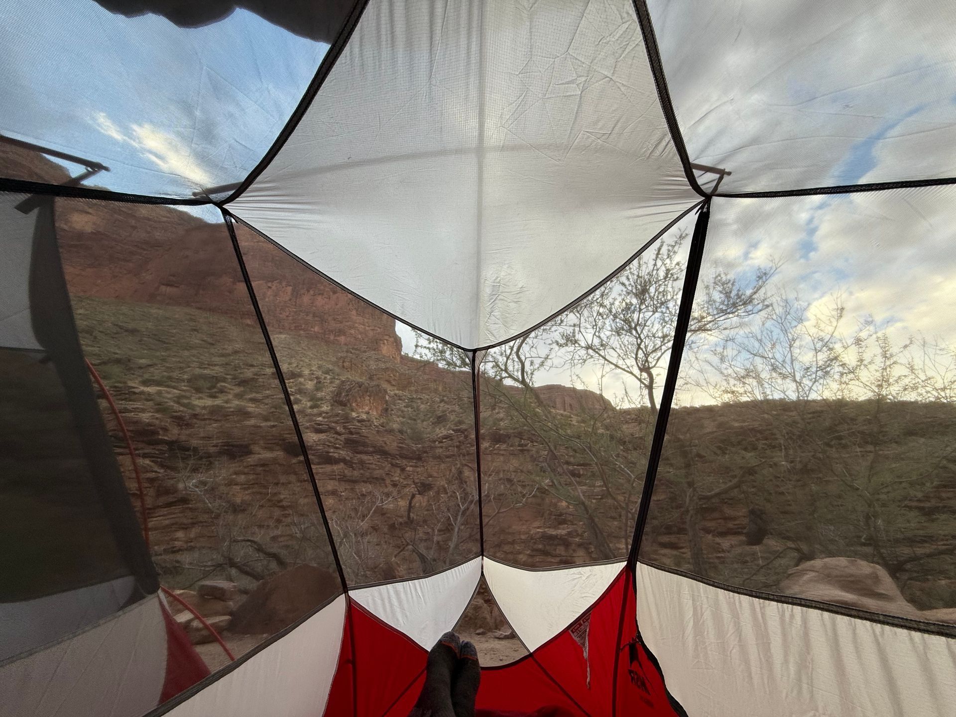 View from inside a tent, looking out at a rocky landscape and cloudy sky. Red and white tent interior.