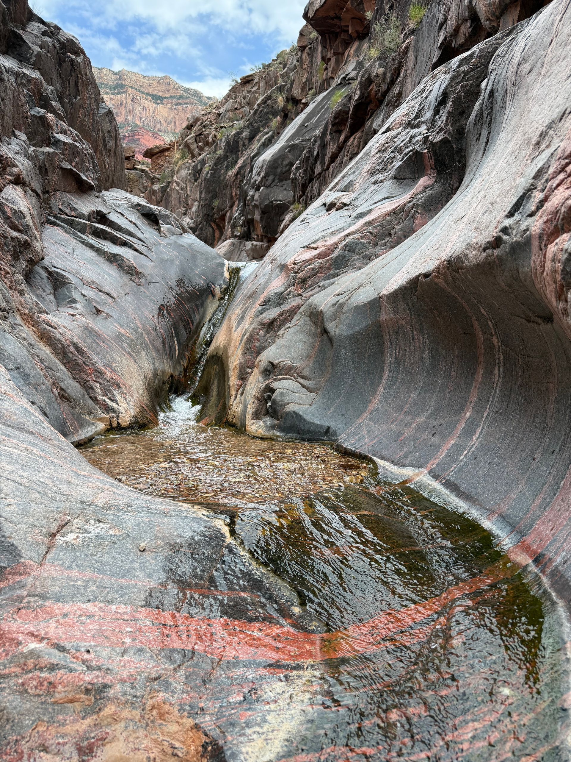 Rocky canyon with a small waterfall and water pooling below. Red and gray layered rock.