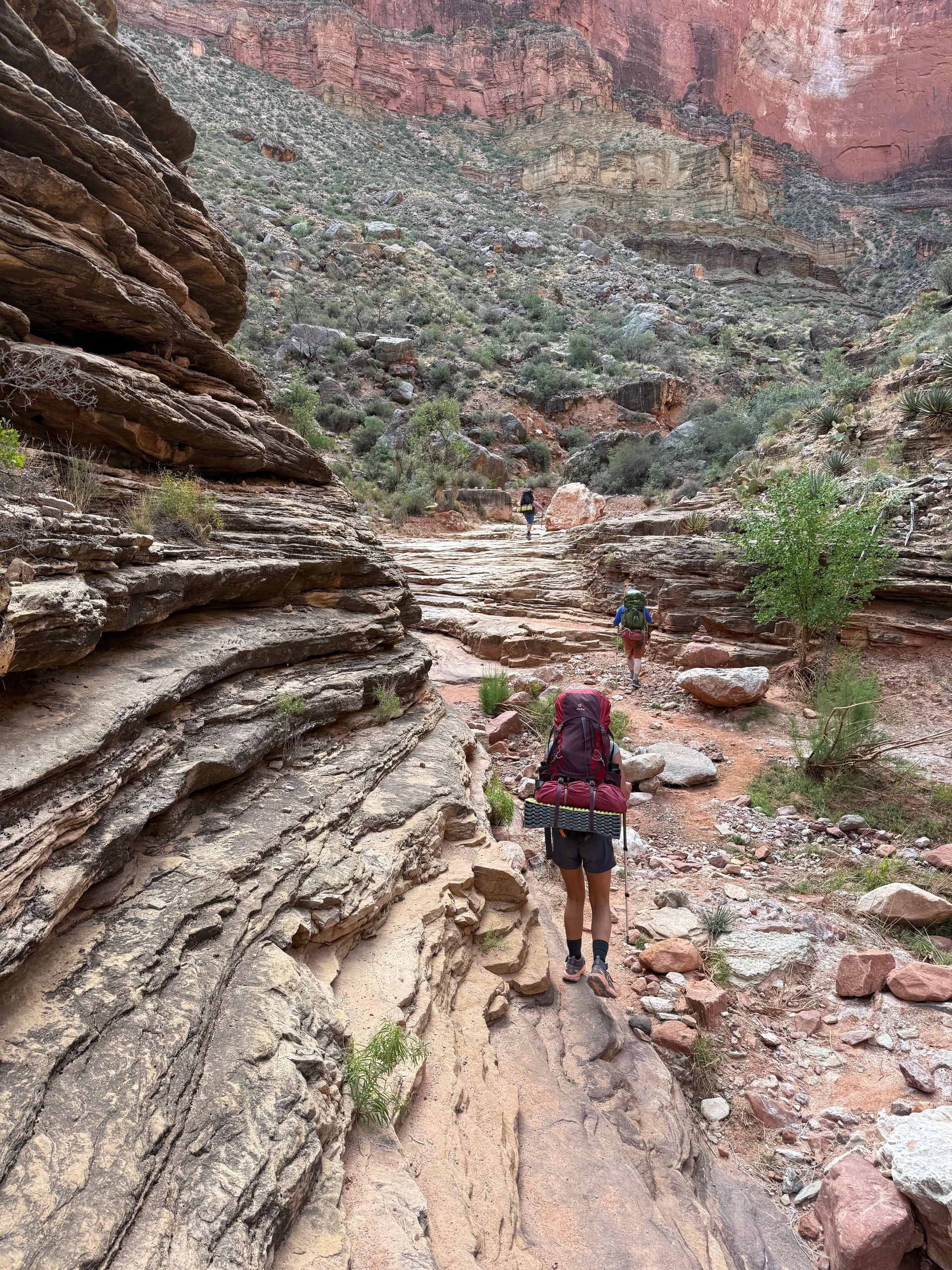 Hikers with backpacks on a rocky trail in a canyon. Red rock walls surround them.