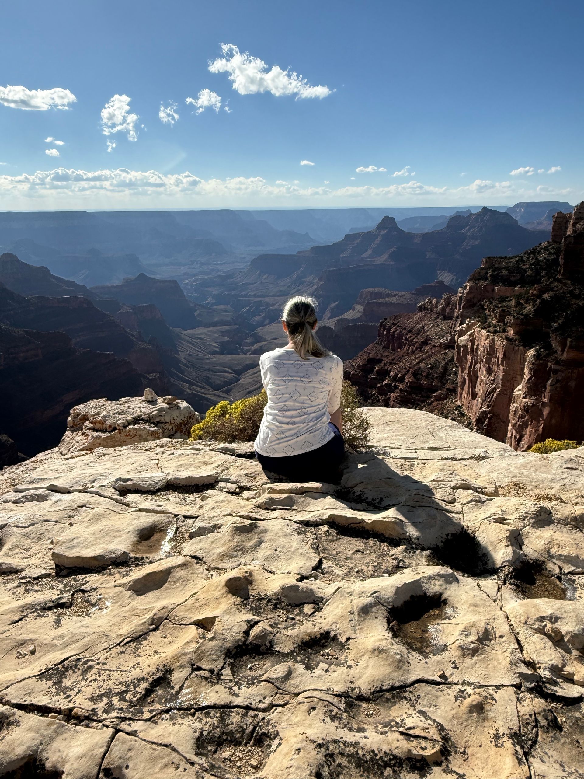 Woman sitting on a rock overlooking the Grand Canyon on a sunny day.