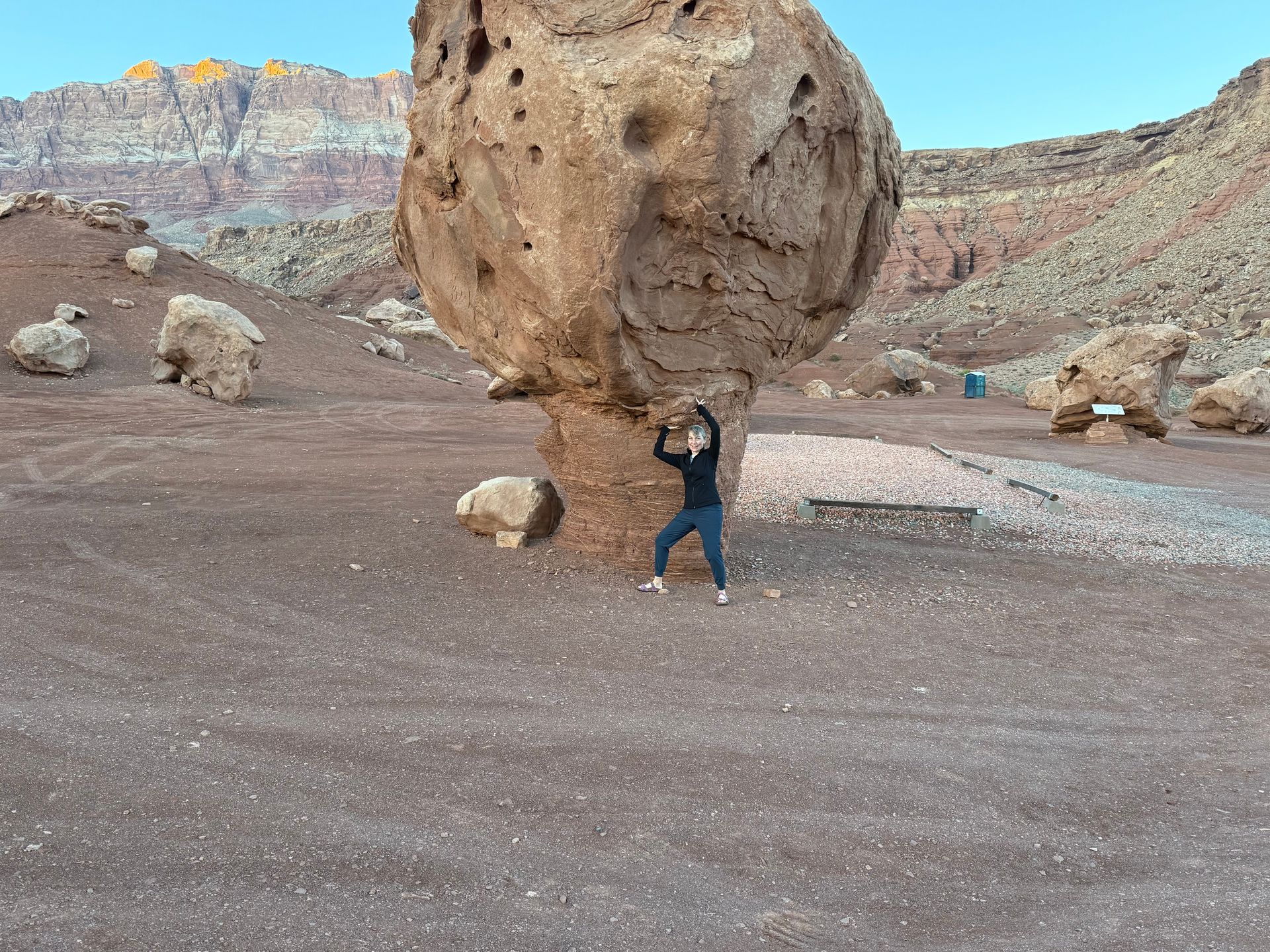Woman lifting a large boulder on a rock pillar in a desert landscape.