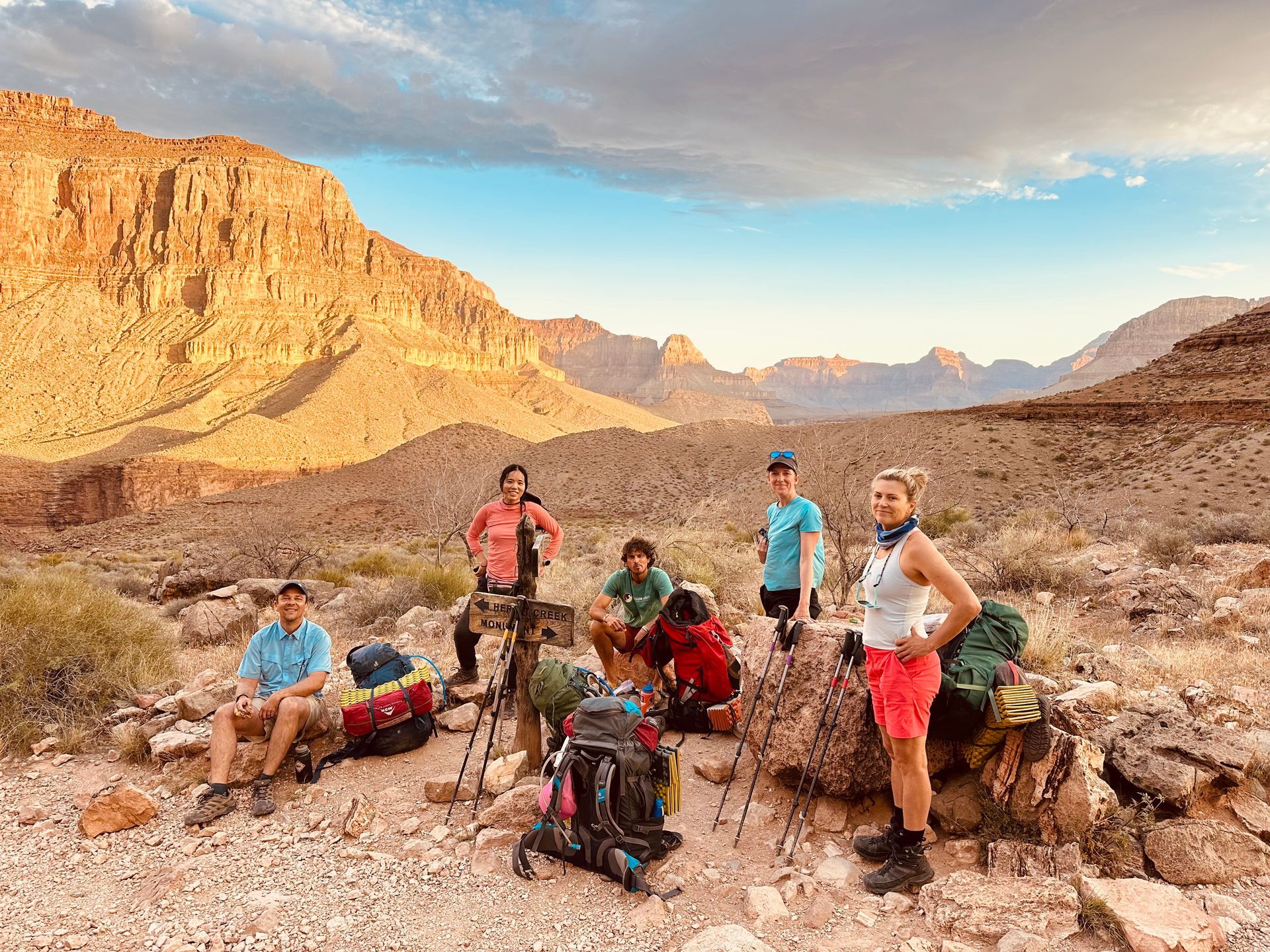 Group of hikers with backpacks in a canyon landscape. Mountains in the background, one person standing.