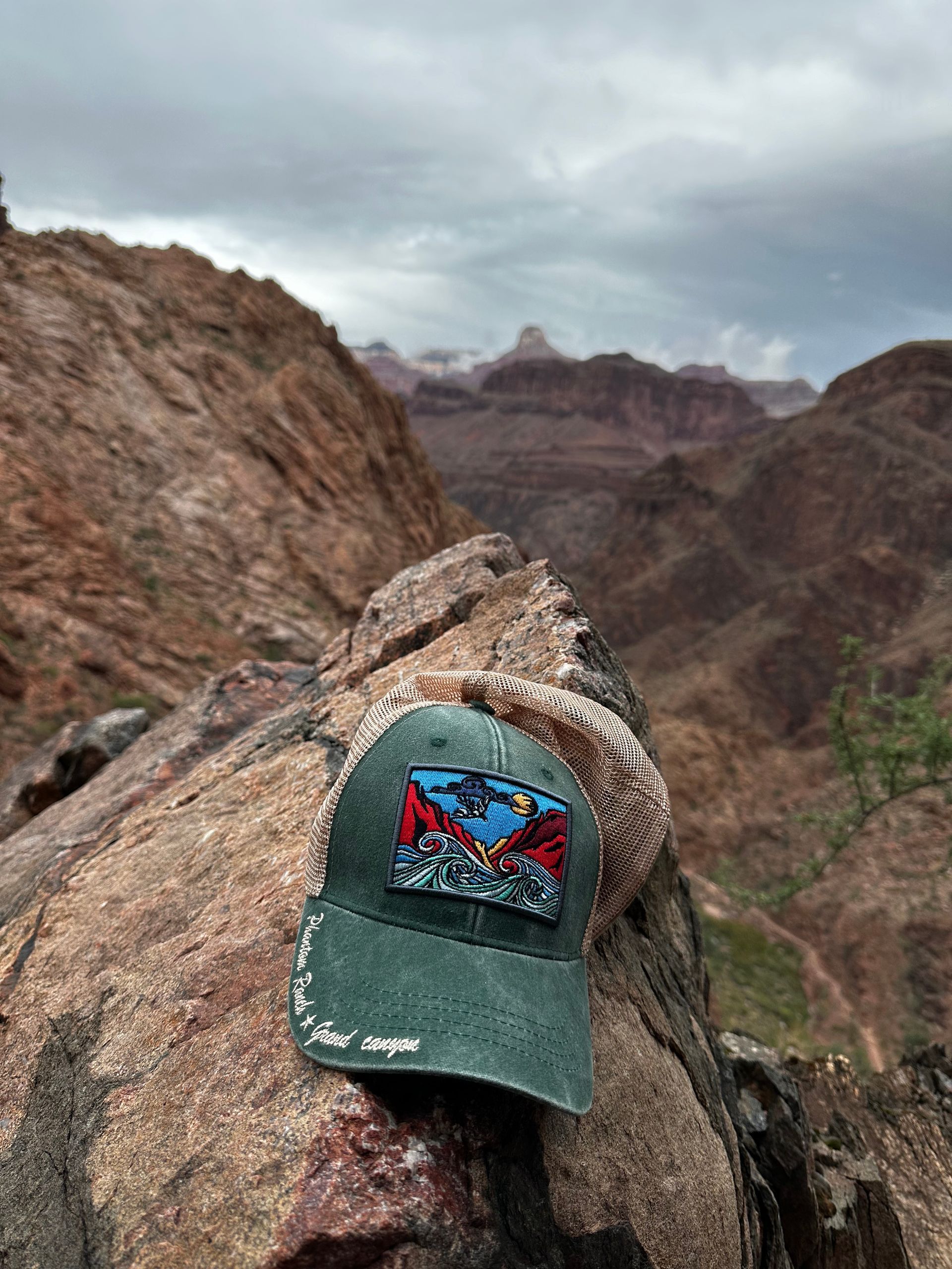 A baseball cap is sitting on top of a rock with mountains in the background.