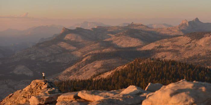 A person is standing on top of a mountain at sunset.