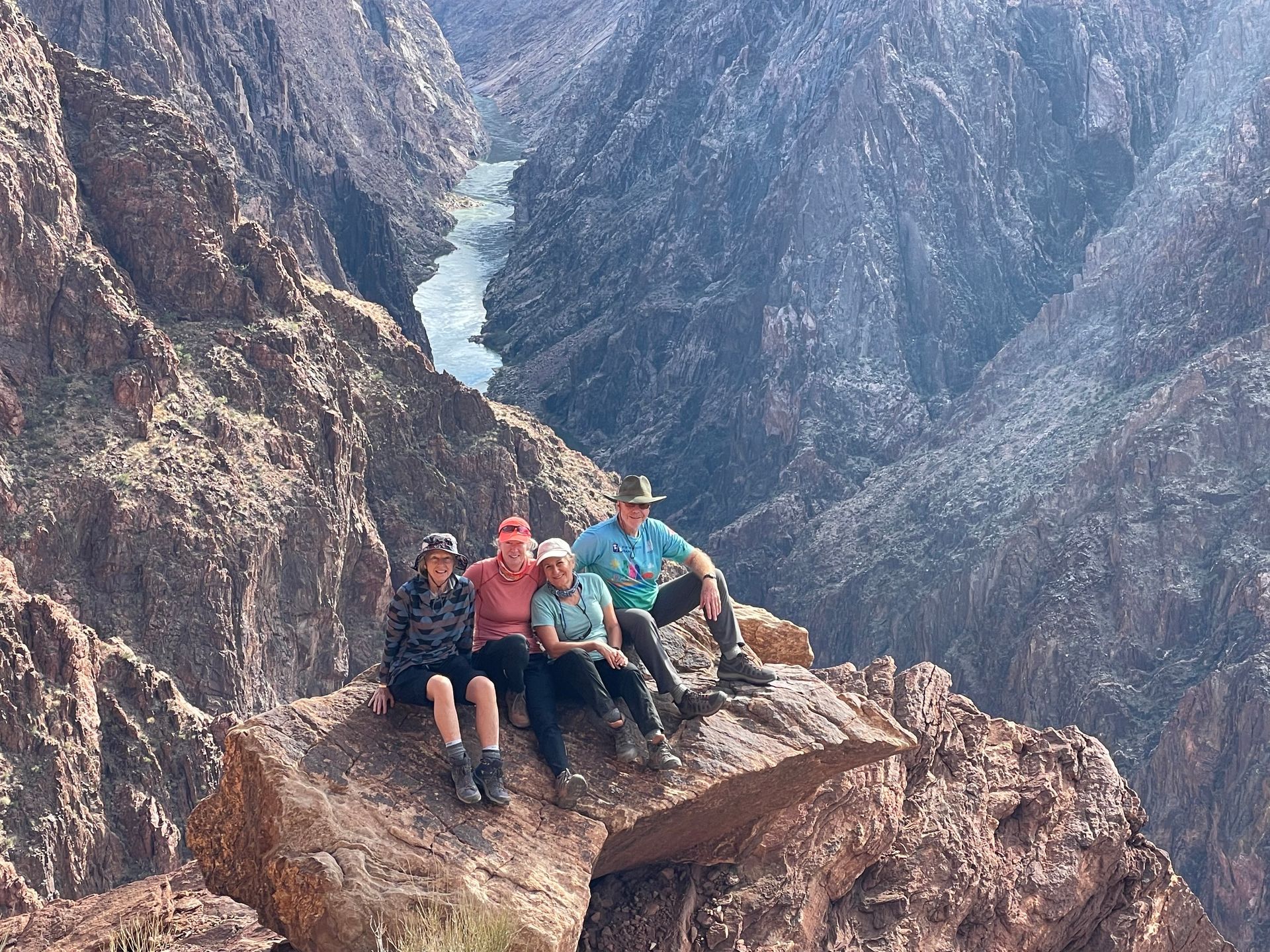 A group of people are sitting on top of a rock in the middle of a canyon.
