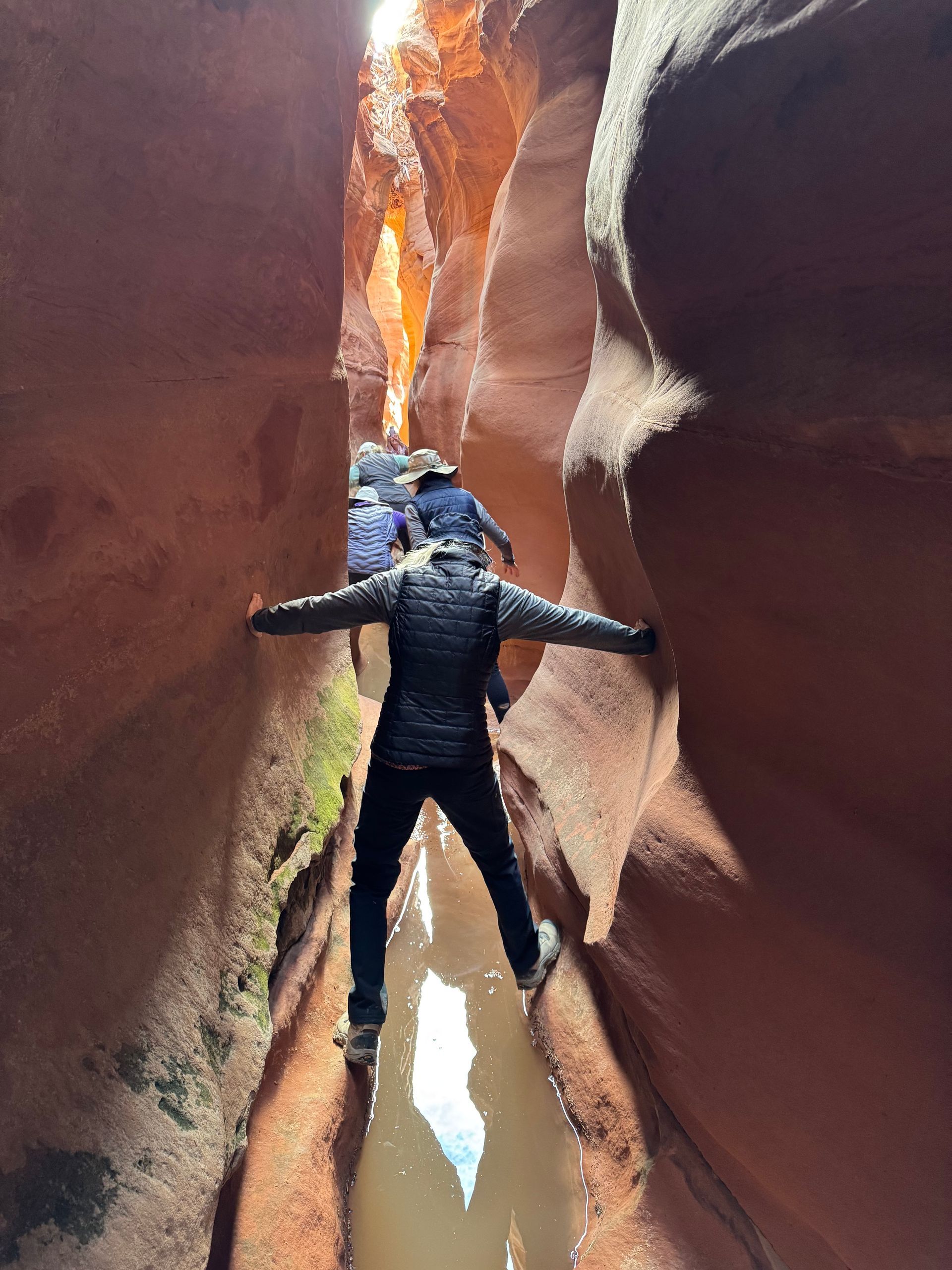 A man is standing in the middle of a canyon with his arms outstretched.