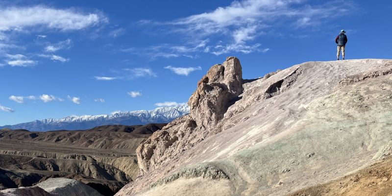 A man is standing on top of a rocky hill in the desert.