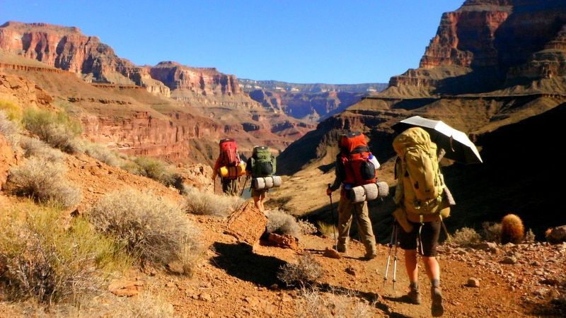 A group of people with backpacks are walking down a trail in the desert