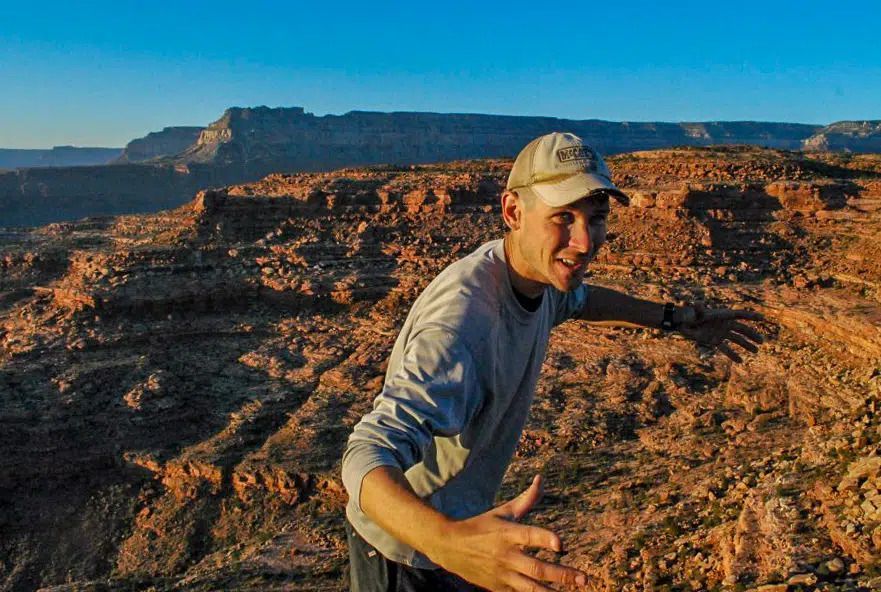 A man in a hat is standing on top of a rocky hill.