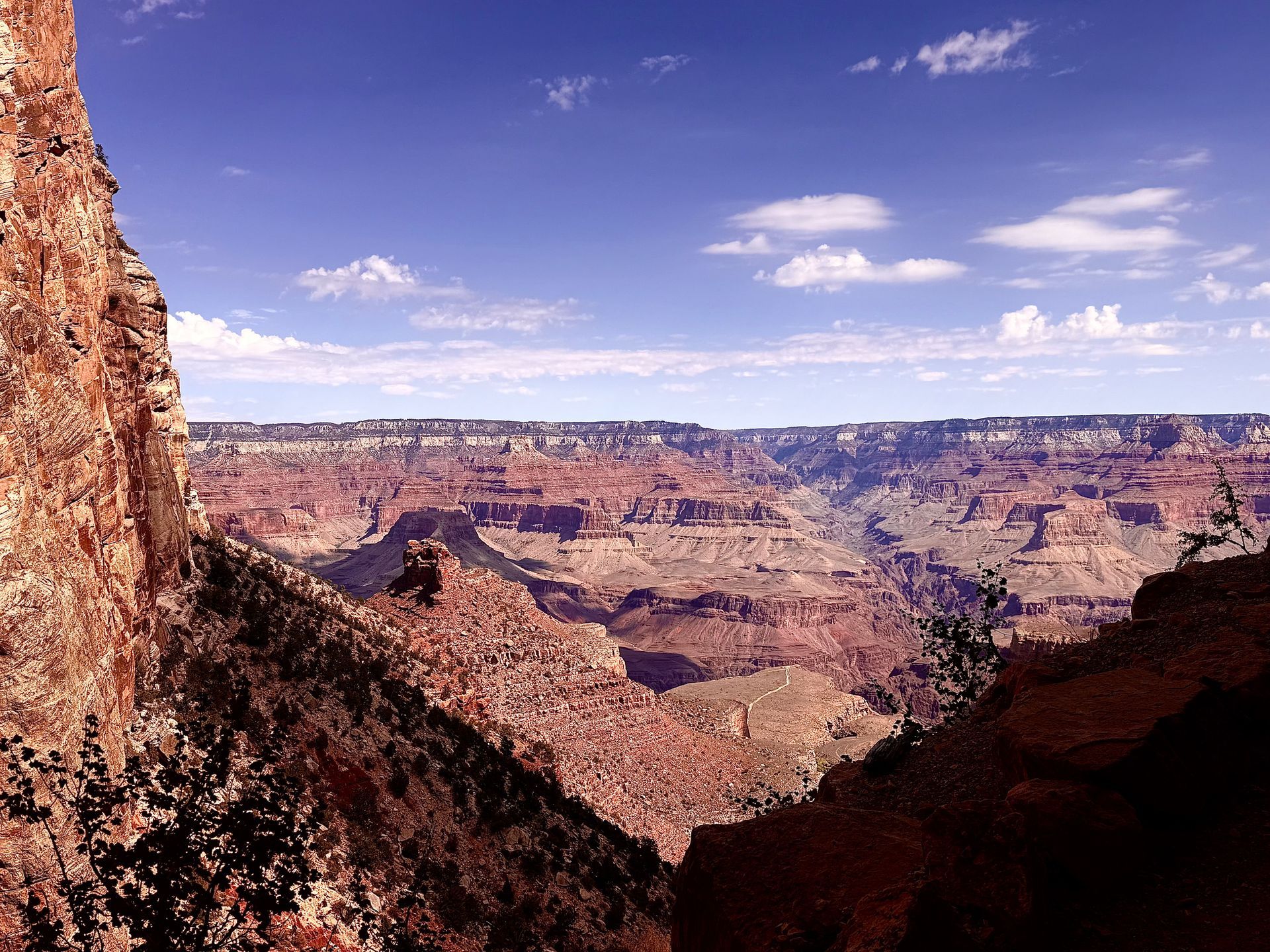 Grand Canyon vista with layered red rock formations under a blue sky with clouds.