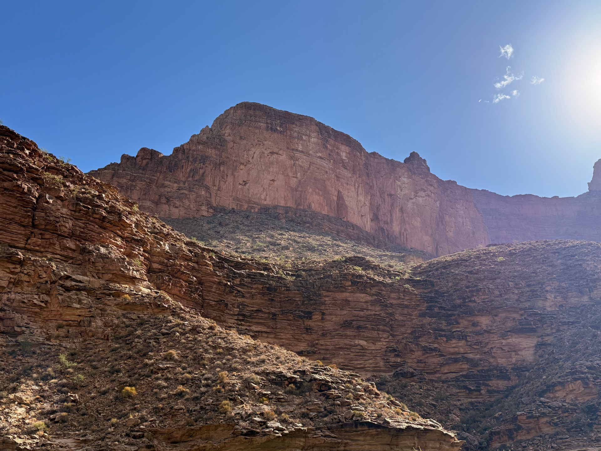 Red rock canyon under a bright blue sky. Sunlight illuminates the cliff face.