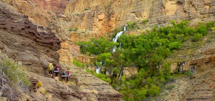 A group of people are walking down a cliff next to a waterfall.