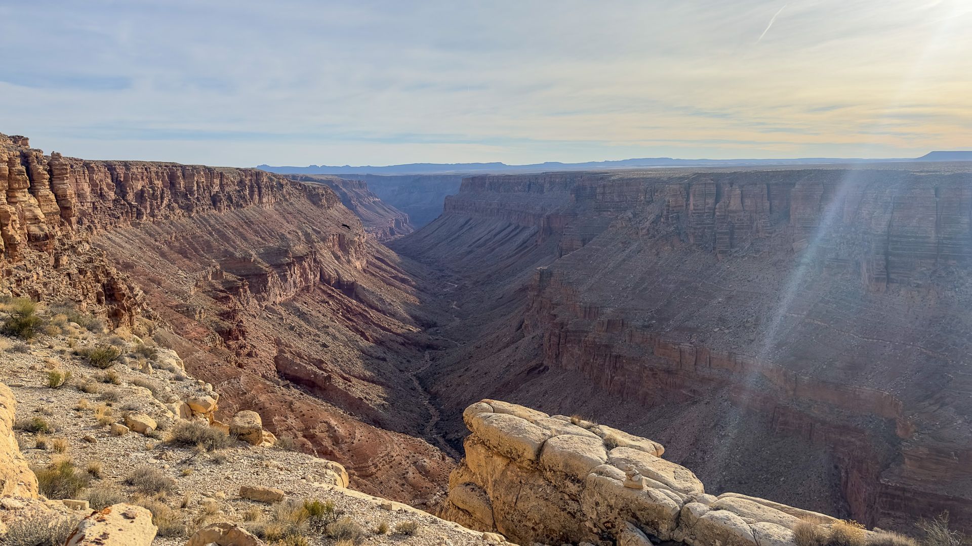 Canyon landscape: deep gorge with layered reddish-brown rock formations under a sunny sky.
